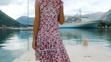 woman in a floral dress walking on a dock by a cruise ship in a harbor