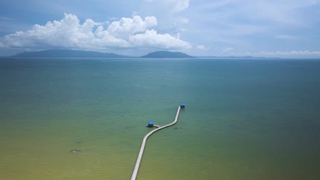 simple calm walking pier to huts jetting out into the blue green ocean with island on the horizon