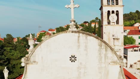 close-up drone view of white stone church facade, rising to reveal bell tower and nerezisce village on brač island, croatia