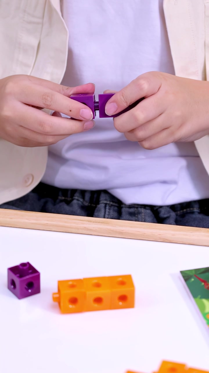 Le mani di un bambino collegano cubi a incastro viola su un tavolo bianco per lo studio della matematica.