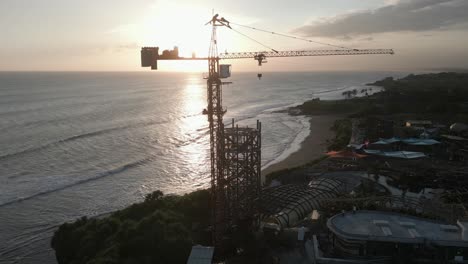 Aerial-orbits-tower-crane-building-tropical-beach-resort-at-sunset
