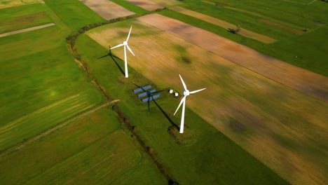 drone shot of two working wind turbines and a few solar panels producing green electric energy on a cultivated field on a sunny summer day, use of renewable resources of energy, still shot