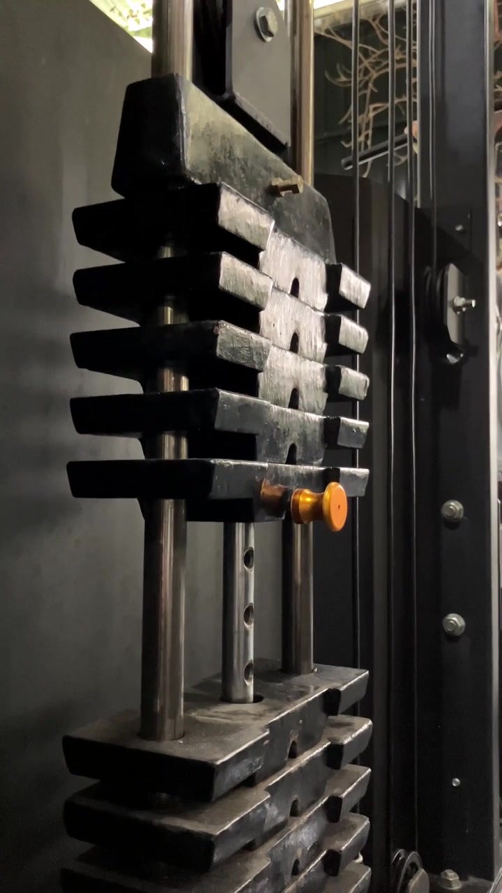 Vertical slow motion video close-up of heavy metal weight stack plates sliding on guide rods during a strength training workout on a cable gym machine.
