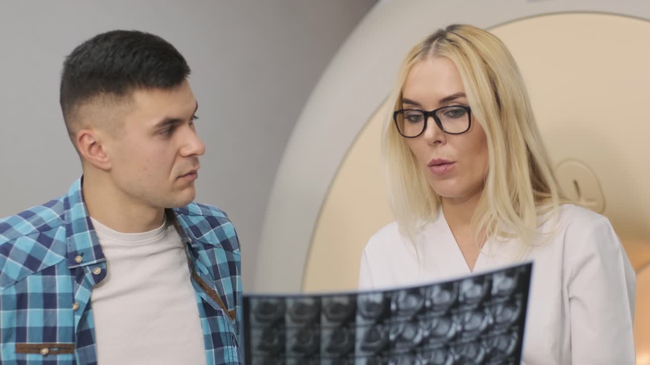 la radióloga explica los resultados de la resonancia magnética para un paciente joven, mostrando la instantánea con imágenes, observando y analizando la resonancia eléctrica en una clínica moderna junto con la mri de tipo cerrado moderna.