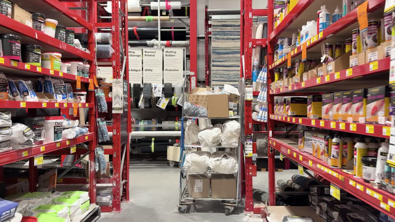Camera moves steadily through hardware store aisle, bright lighting, shelves stocked with paint, tiles, supplies