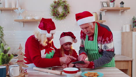 Senior-grandparents-and-grandchild-watching-cooking-lesson-using-digital-tablet-at-Christmas-kitchen