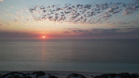 Sunset-over-the-horizon-aerial-shot-from-the-seashore-towards-the-sea-with-cloudy-sky,-drone-orbital-shot