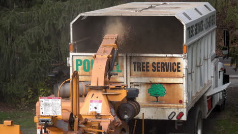 wood chips are expelled from the chute of a wood chipper into a truck bed