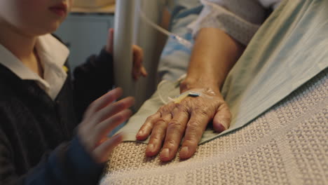 little boy touching hand of grandmother lying in hospital bed child showing affection at bedside for granny recovering from illness health care support