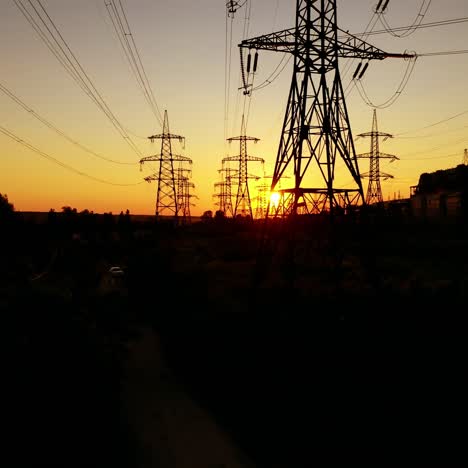 power station near the river at sunset. tall silhouettes of high-voltage electric lines in the evening. electric towers on orange background of the setting sun.