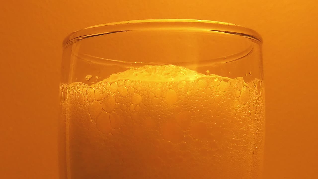 primer plano de espuma de cerveza en vidrio contra fondo naranja