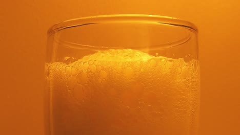 Close-up-of-beer-foam-in-glass-against-orange-background