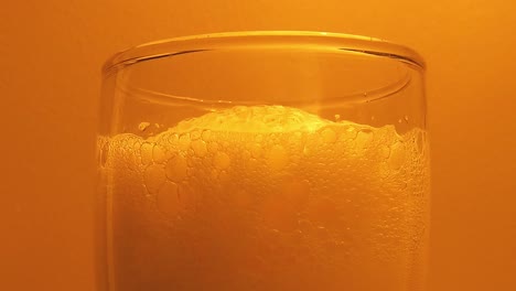 close up of beer foam in glass against orange background