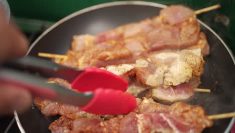 tongs moving chicken skewers cooking over a hot frying pan