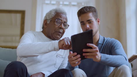 bearded caucasian guy helping senior black man with using tablet