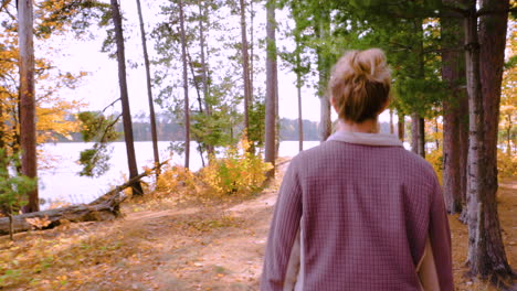 woman hiking on a path through autumn forest to a lake