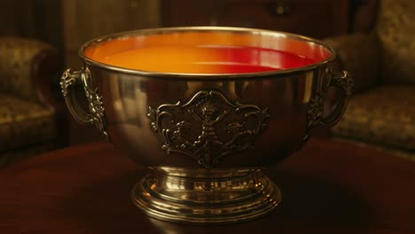 a stunning antique silver bowl filled with vibrant orange and red liquid, expertly crafted with intricate design elements and captured in a cozy setting