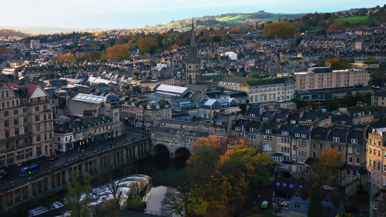 Perspectiva aérea aproximada de drone do Rio Avon em cascata sobre a barragem na Ponte Pulteney, na histórica cidade de Bath, Inglaterra, durante um colorido pôr do sol de outono.
