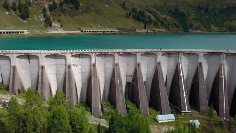 Muro-De-La-Presa-Del-Lago-Fedaia-En-Las-Montañas-Dolomitas-Del-Norte-De-Italia-Con-Personas-Y-Autos-Moviéndose-En-La-Parte-Superior,-Un-Dron-Aéreo-Revela-Un-Disparo-A-La-Izquierda