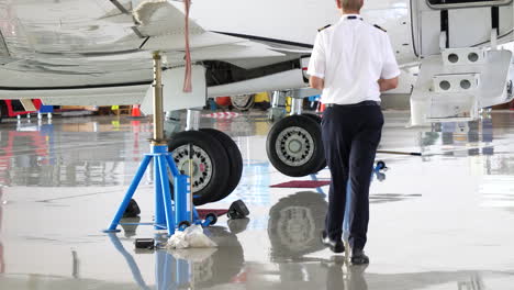 Pilot-walks-towards-jet-airplane-on-jacks-during-maintenance-in-hangar