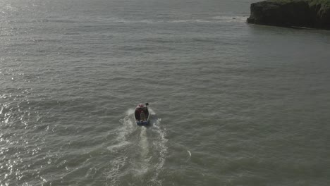 Tracking-aerial-of-small-open-crab-boat-motoring-to-trap-by-sea-cliff