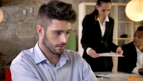 young concentrated businessman is in office, watching at camera, smiling, people are networking with technologies, working concept, business concept, communication concept, blurred background