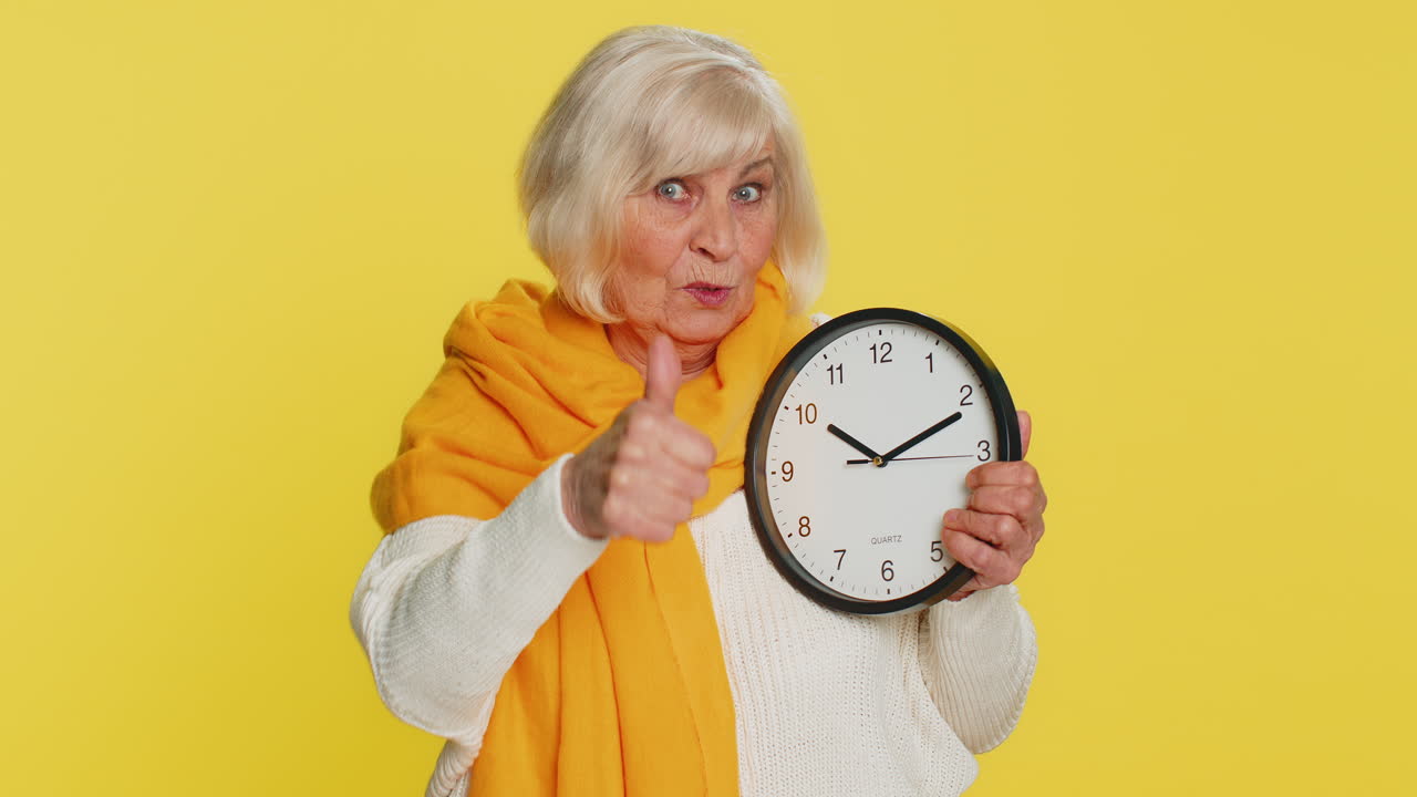 Vecchia donna anziana che mostra l'ora sull'orologio da ufficio al muro ok pollice in alto approva sbrigati scadenza