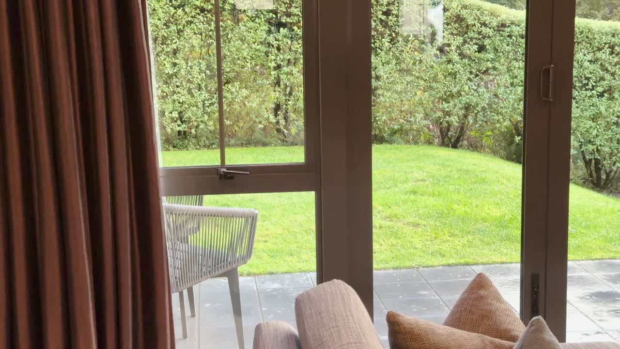 Camera pans from a bright garden patio through sliding glass doors into a warm living room, ending on a lit stone gas fireplace and TV