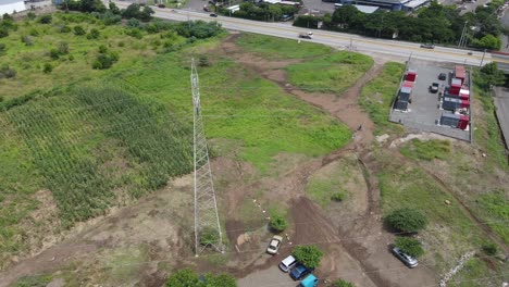 Aerial-view-around-a-high-voltage-electric-power-tower-in-the-middle-of-a-farm-field-near-a-main-road
