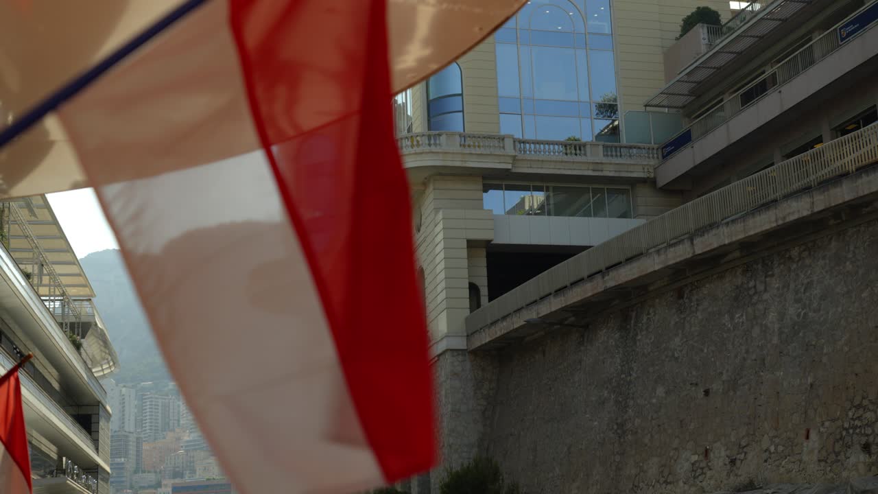 Flags waving near iconic architecture in Monte Carlo, Monaco, with a scenic backdrop of city buildings and hills. Capturing a vibrant urban atmosphere with a touch of national pride.