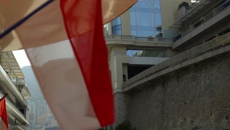 Flags waving near iconic architecture in Monte Carlo, Monaco, with a scenic backdrop of city buildings and hills. Capturing a vibrant urban atmosphere with a touch of national pride.