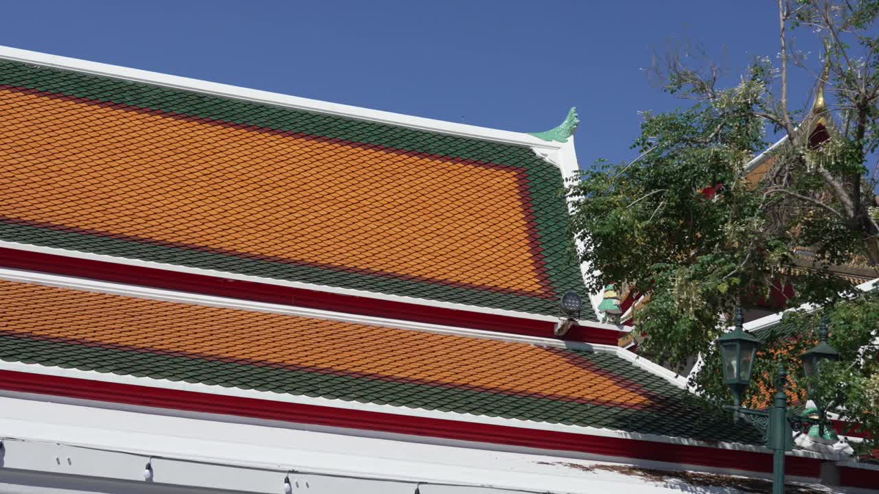 Close-up view of the ornate roof of Wat Pho in Bangkok, Thailand, showcasing traditional Thai temple design, vivid colors, and intricate craftsmanship under a clear blue sky