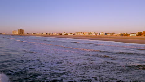 Volando-Sobre-El-Océano-Hacia-La-Playa-De-Jersey-Shore-Al-Amanecer-Con-Casas-Al-Fondo