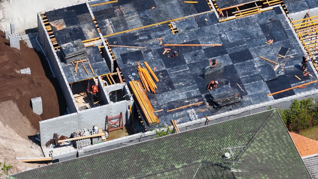 Drone aerial shot of construction workers preparing concrete slab formwork on sunny residential building site