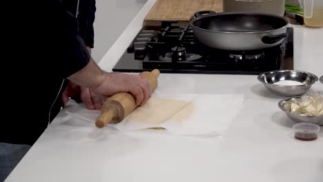 a person skillfully rolls out dough on a clean countertop, preparing for a delicious savory dish. ingredients are neatly arranged nearby including butter, sugar, and vanilla