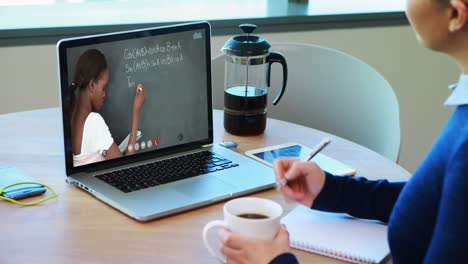 Caucasian-female-student-using-laptop-on-video-call-with-female-teacher,-making-notes