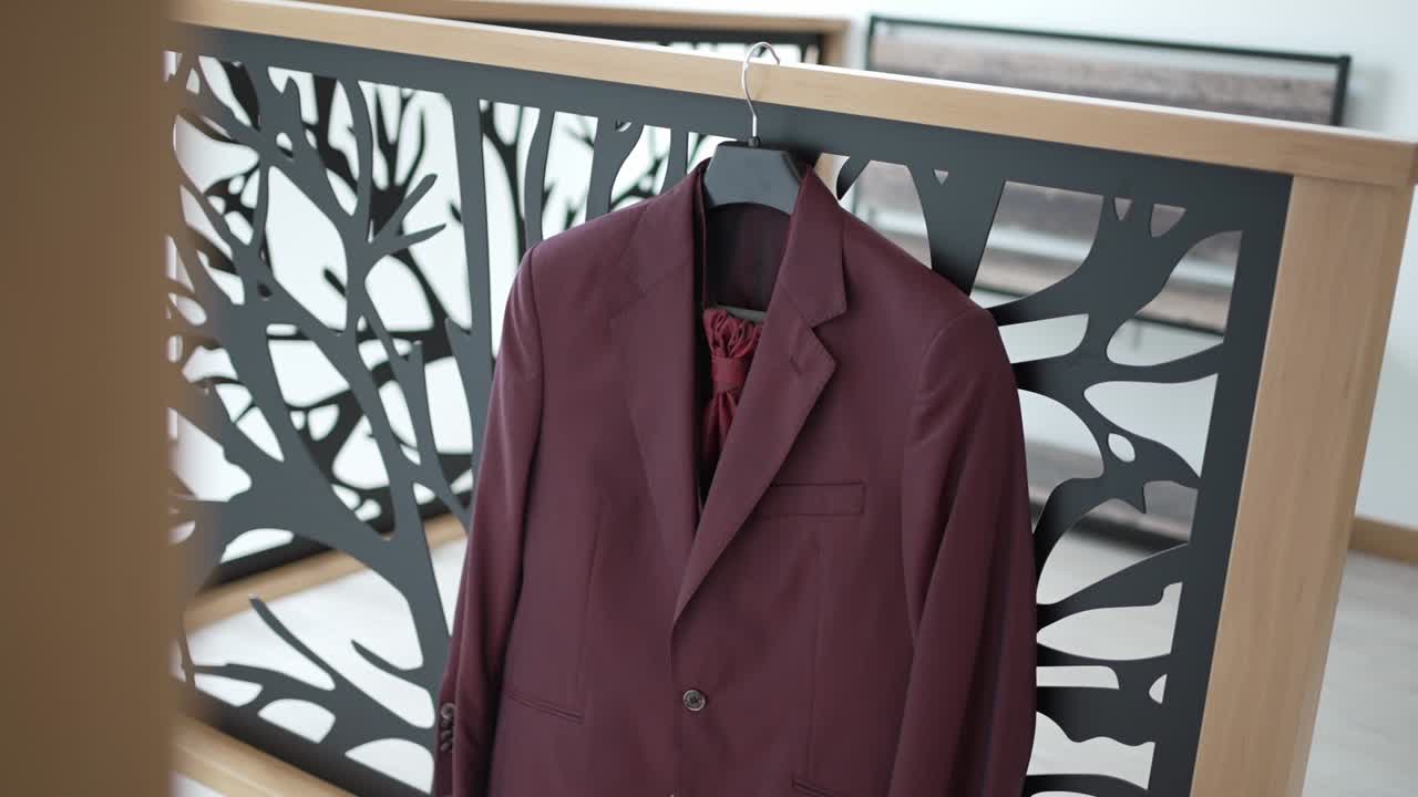 Elegant burgundy suit with matching tie hanging on a modern railing indoors