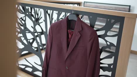 elegant burgundy suit with matching tie hanging on a modern railing indoors