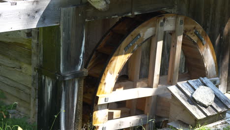 close up shot of old wooden water mill rotating in mountains of switzerland during sun - a watermill or water mill is a mill that uses hydropower