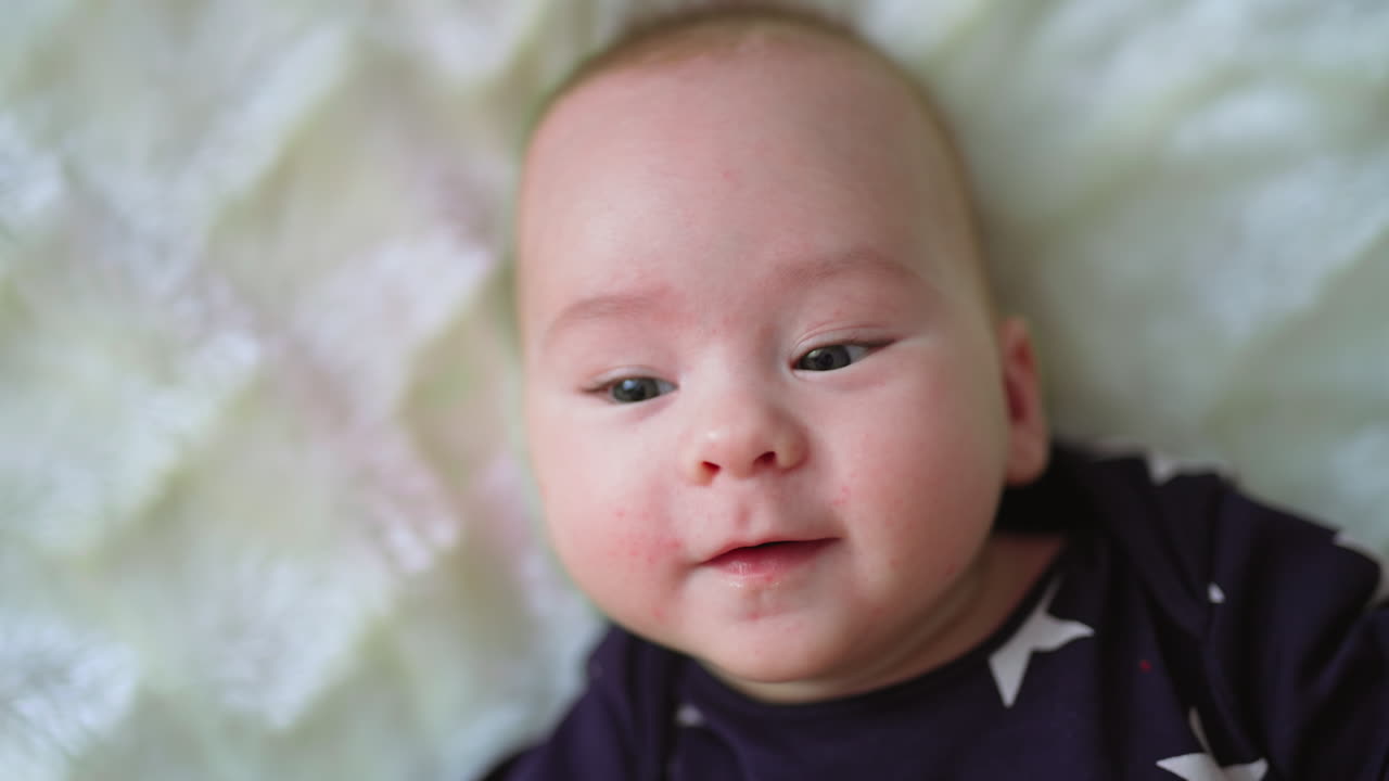 Adorable baby boy smiling sweetly to the camera. Mom's hand caresses tender boy's cheek with love and care. Close up.