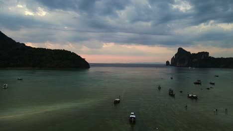 Bester-Luftbildflug-Einer-Tropischen-Insel-Bei-Sonnenuntergang-Und-Bewölktem-Himmel-Mit-Booten,-Die-Auf-Einem-Türkisfarbenen-Meer-Segeln