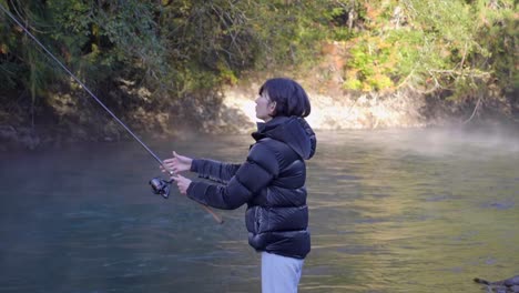 bank fishing - woman throwing bait into the water, angling with fishing rod in the river