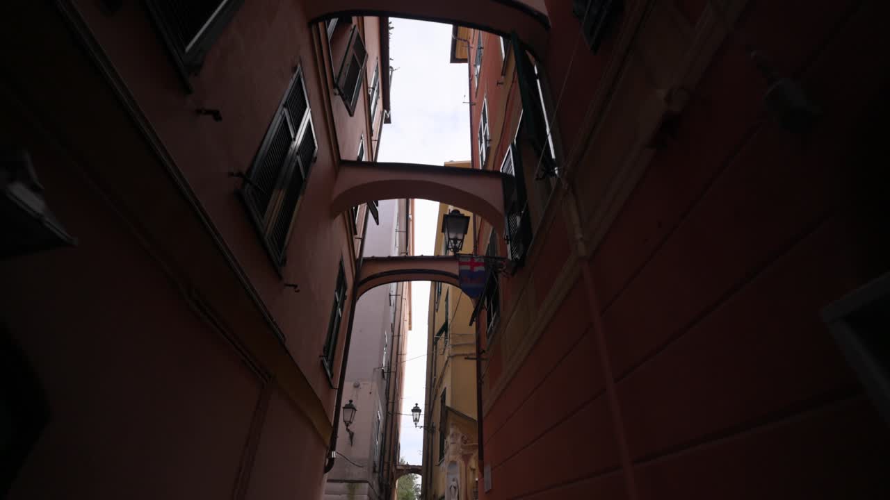Punto di vista dal basso camminando attraverso un caruggio, un tipico vicolo stretto con archi, nel centro storico di Varazze, Italia. Vista in prima persona