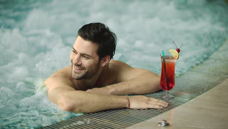 portrait of sexy guy relaxing in pool at spa hotel. happy man posing in jacuzzi