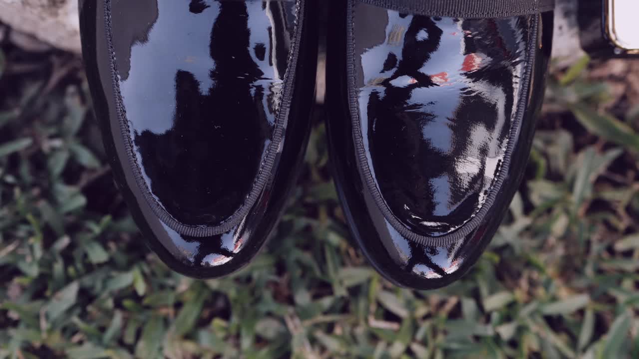 Close up of glossy black dress shoes reflecting trees on grass
