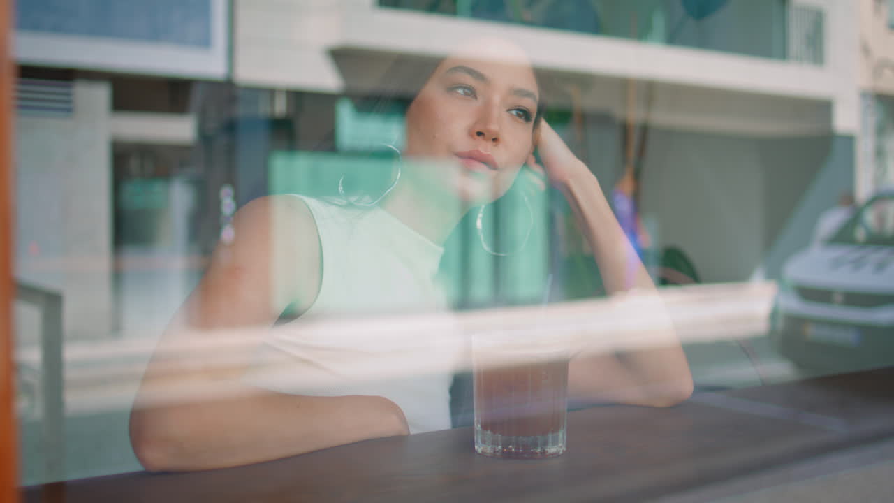 지루한 여자가 카페에 앉아 도시 거리의 창문을 통해 가까이보고 있습니다.
