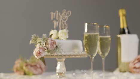 Wedding-Cake-With-Glasses-Of-Champagne-Against-Grey-Studio-Background-At-Wedding-Reception