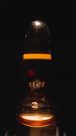 glass ampule with brown liquid and long tip reflecting studio light on black background. sealed vial used to contain and preserve sample macro