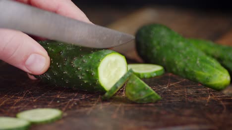 male hand with a knife cut the cucumber into pieces.