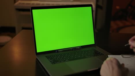 un hombre se prepara para tomar notas aprendiendo en línea en una computadora portátil con una pantalla verde
